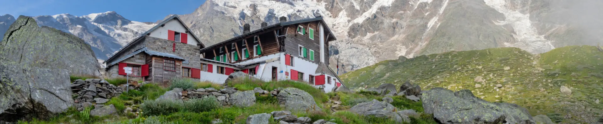 Stone mountain hut with red shutters below a glacier