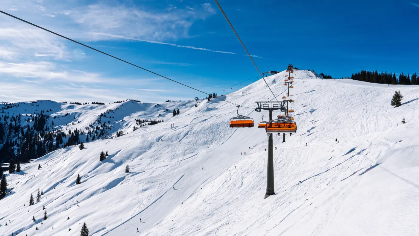 Chairlift with orange chairs above snowy slopes