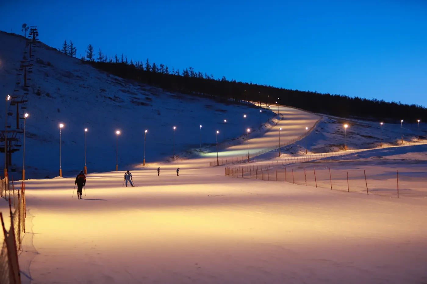 Ski slope lit up at night with a few skiers